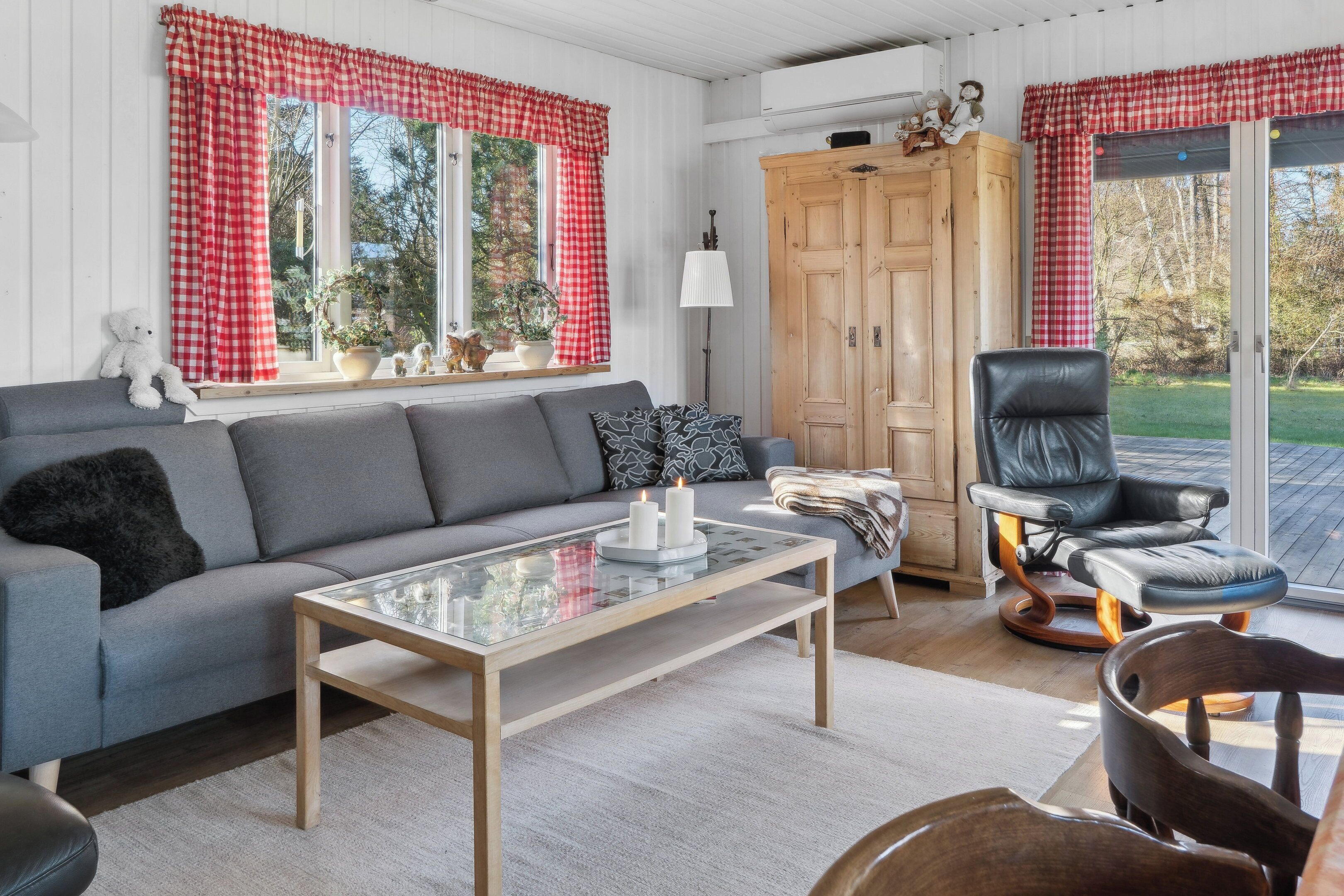 Een gezellige woonkamer met een grijze bank, een glazen salontafel, een houten kast en een zwarte leren fauteuil.