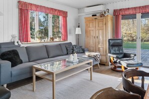 Ein gemütliches Wohnzimmer mit grauem Sofa, einem Glastisch, einem Holzschrank und einem schwarzen Ledersessel.