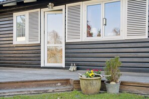 A wooden house with a porch, a window with shutters, and a potted plant.