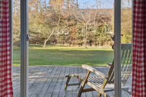 Eine Holzterrasse mit einer Bank, einer Glastür und Blick auf einen Rasen mit Bäumen.
