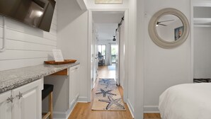 Un pasillo con un tapete estampado con motivos de estrellas de mar, un espejo redondo y una cocina con una campana extractora de acero inoxidable.