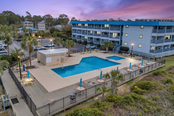 A hotel with a large outdoor pool, multiple balconies, and a parking area.