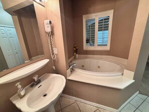 A bathroom with a sink, a bathtub, and a window with blinds.