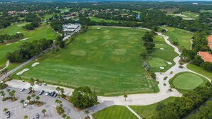 An aerial view of a golf course with multiple holes, a parking area, and surrounding greenery. - Right Direction Rentals 1 Bedroom Villa 9906 (Port St. Lucie)