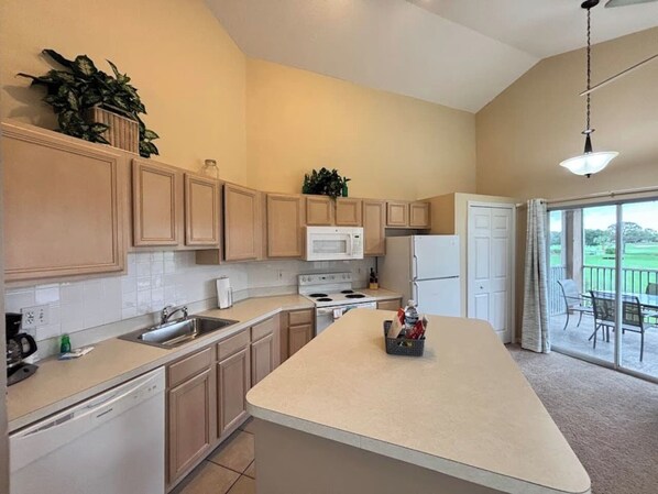 A kitchen with wooden cabinets, a microwave, a refrigerator, and a large island.