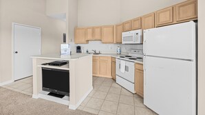 A modern kitchen with wooden cabinets, a microwave, a refrigerator, and a built-in oven. - Right Direction Rentals 1 Bedroom Villa 9906 (Port St. Lucie)
