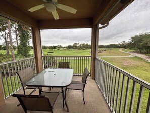 A covered outdoor area with a table and chairs, a ceiling fan, and a view of a green landscape.