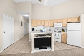 A compact kitchen with a microwave, stove, refrigerator, and a small entertainment unit.
