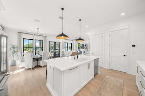 Une cuisine moderne dotée d’un îlot central, de luminaires suspendus et offrant une vue sur l’extérieur.