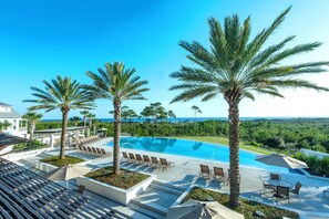 A pool area with palm trees, lounge chairs, and a view of the ocean.