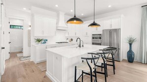A modern kitchen with white cabinetry, a central island, black bar stools, and pendant lighting. - ☀️Infinity Pool-4BR-30A Cypress Stay (Santa Rosa Beach)