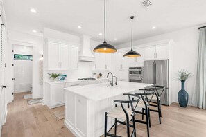 A modern kitchen with white cabinetry, a central island, black bar stools, and pendant lighting.