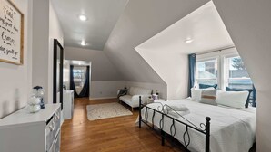 A bedroom with a sloped ceiling, a bed with white bedding, a white dresser, a bedside table, and a window with blinds.