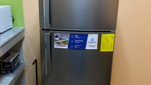 Ein Edelstahl-Kühlschrank mit einem blauen und gelben Aufkleber an der Tür, platziert in einer Küche mit grüner Wand und gefliestem Boden.