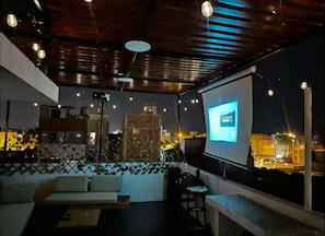 A rooftop terrace with a seating area, a projector screen, and a city view.