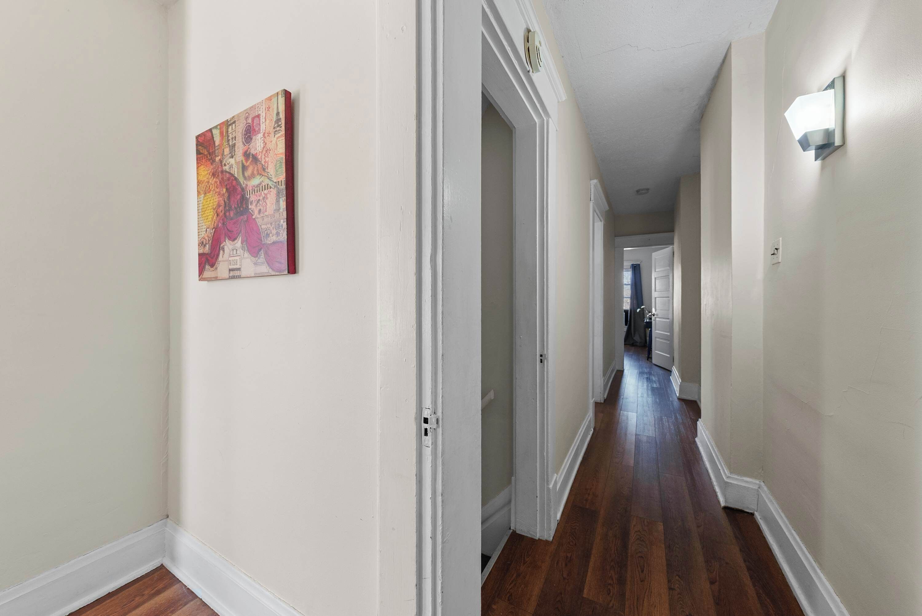 A hallway with white walls, a wooden floor, and a door leading to another room.