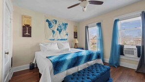 Une chambre à coucher avec un lit, un pouf bleu, un ventilateur de plafond, une carte du monde et une fenêtre avec des rideaux.