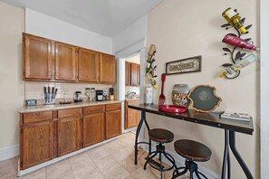 Una cocina con armarios de madera, una encimera con diversos utensilios de cocina, un cartel de degustación de vinos y una mesa con taburetes.