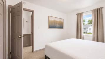 Une chambre à coucher avec un lit, une porte, un tableau et une fenêtre avec des rideaux.