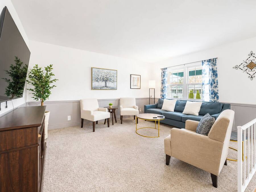 A living room with a flat-screen TV, a sofa, a chair, a coffee table, and a plant.