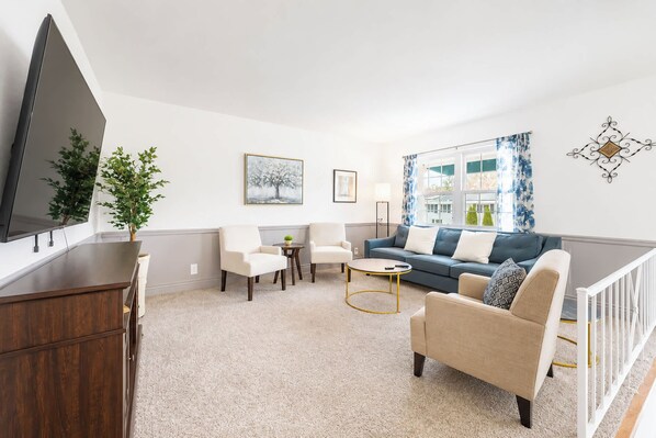 A living room with a flat-screen TV, a sofa, a chair, a coffee table, and a plant. - Easton 4BR Getaway Game Room + 2 Living Areas (Columbus)
