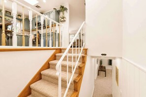 Un escalier dont les marches sont recouvertes de moquette et qui possède des rampes blanches, menant à un deuxième étage.