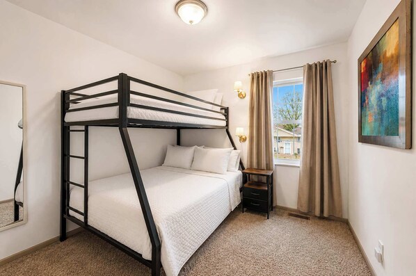 A bunk bed room with a window, a nightstand, and a painting on the wall. - The Gahanna Getaway (Columbus)