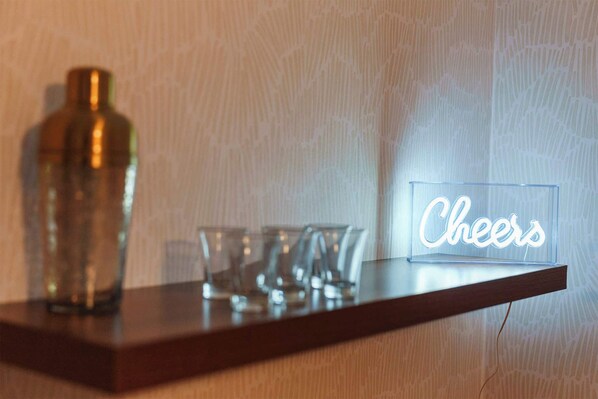A wooden shelf with a clear bottle, a glass, and a neon sign that reads 'Cheers'. - The Gahanna Getaway (Columbus)