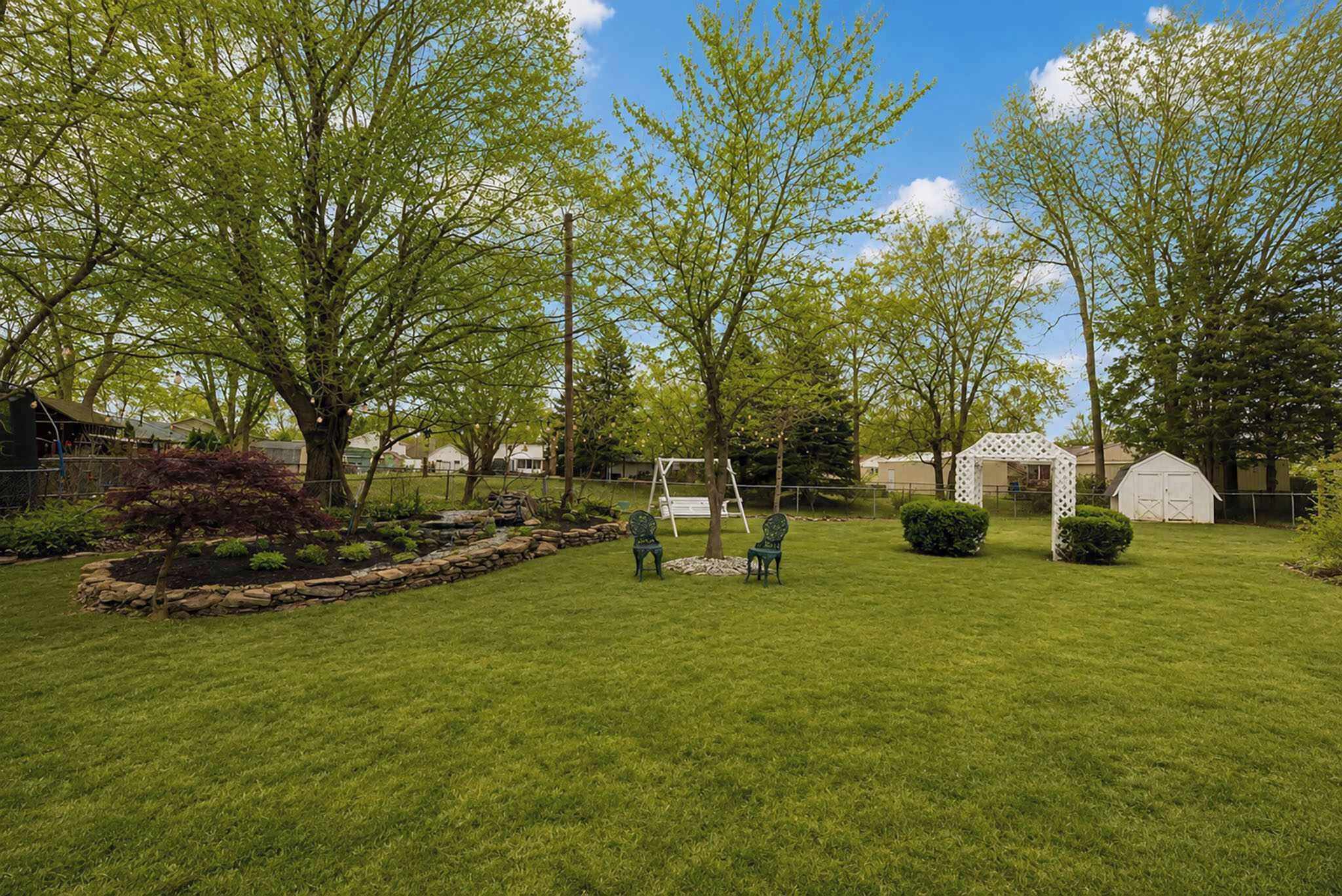 A well-maintained grassy yard with a swing set, a small shed, and a garden area with a stone border.
