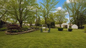 A well-maintained grassy yard with a swing set, a small shed, and a garden area with a stone border.