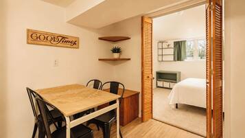A room with a dining table, chairs, a bed, a TV, and a door leading to another room.