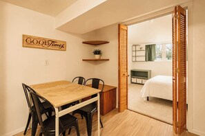 A room with a dining table, chairs, a bed, a TV, and a door leading to another room. - The Gahanna Getaway (Columbus)