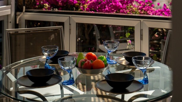 Une table en verre avec vue sur la mer et agrémentée de fleurs roses.