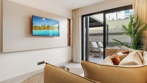 A modern living room with a large flat-screen TV mounted on the wall, a sofa with cushions, a potted plant, and a sliding glass door leading to an outdoor area. - Stylish 2BR in Estepona, Walk to Beach & Old Town (Estepona)