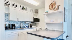 Une cuisine moderne avec des meubles blancs, un îlot central et un tabouret de bar bleu.