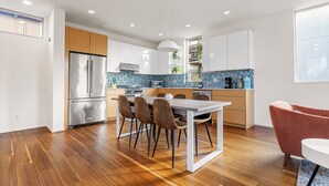 A modern kitchen with wooden flooring, a stainless steel refrigerator, a dining table with chairs, and a red chair. - The Rooftop Blue Haven Home w Firepit (Seattle)
