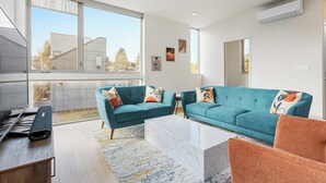 A modern living room with teal sofas, a marble coffee table, and large windows offering a view of the neighborhood. - The Rooftop Blue Haven Home w Firepit (Seattle)