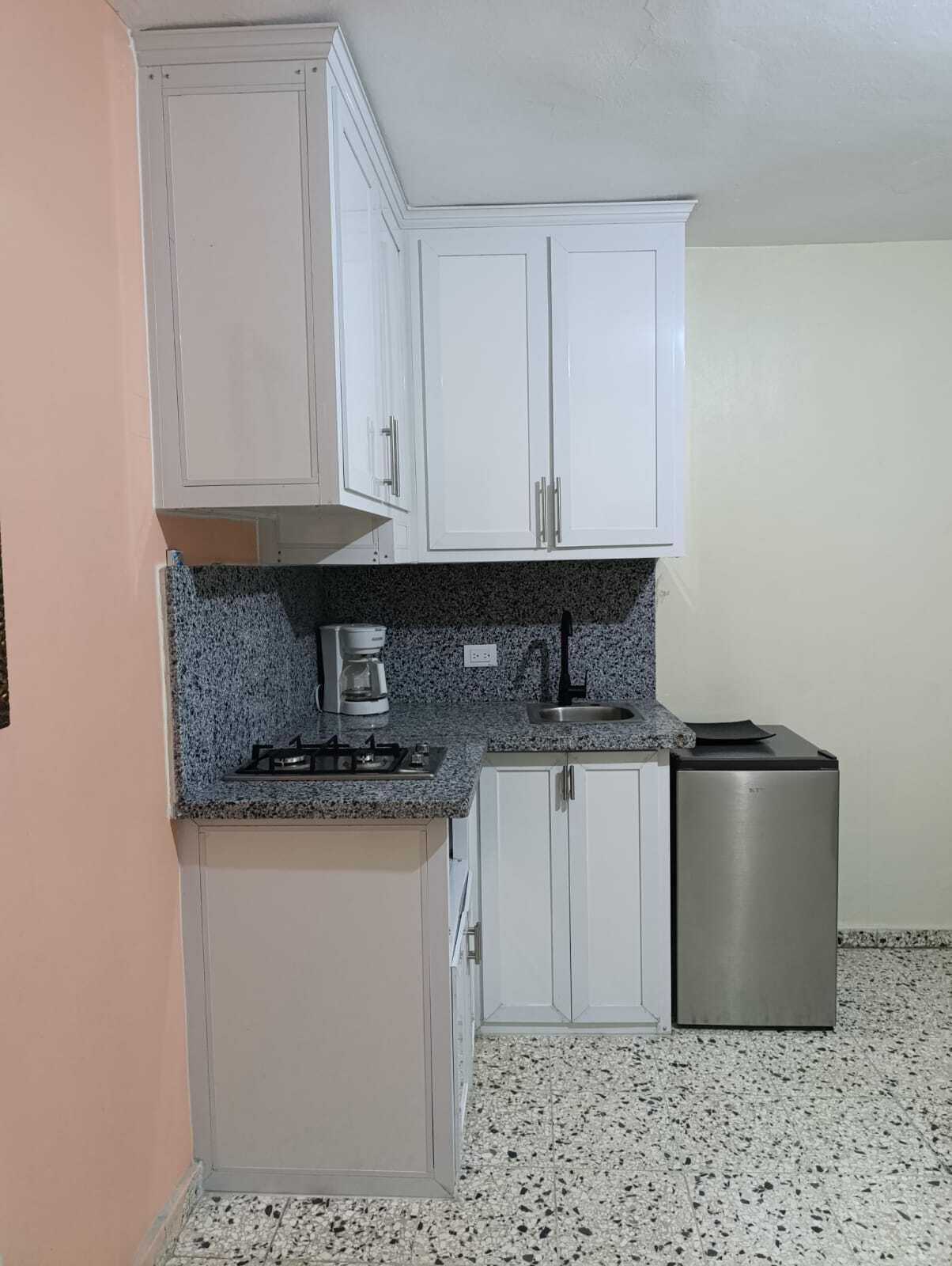 A compact kitchen with white cabinets, a granite countertop, a gas stove, a coffee maker, and a stainless steel refrigerator.