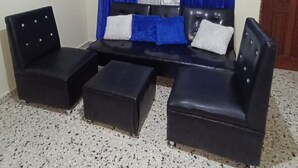 A room with a black sofa set, two black armchairs, and a matching ottoman.