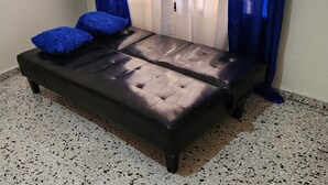 A black leather sofa with two blue cushions, a tiled floor, and blue curtains.