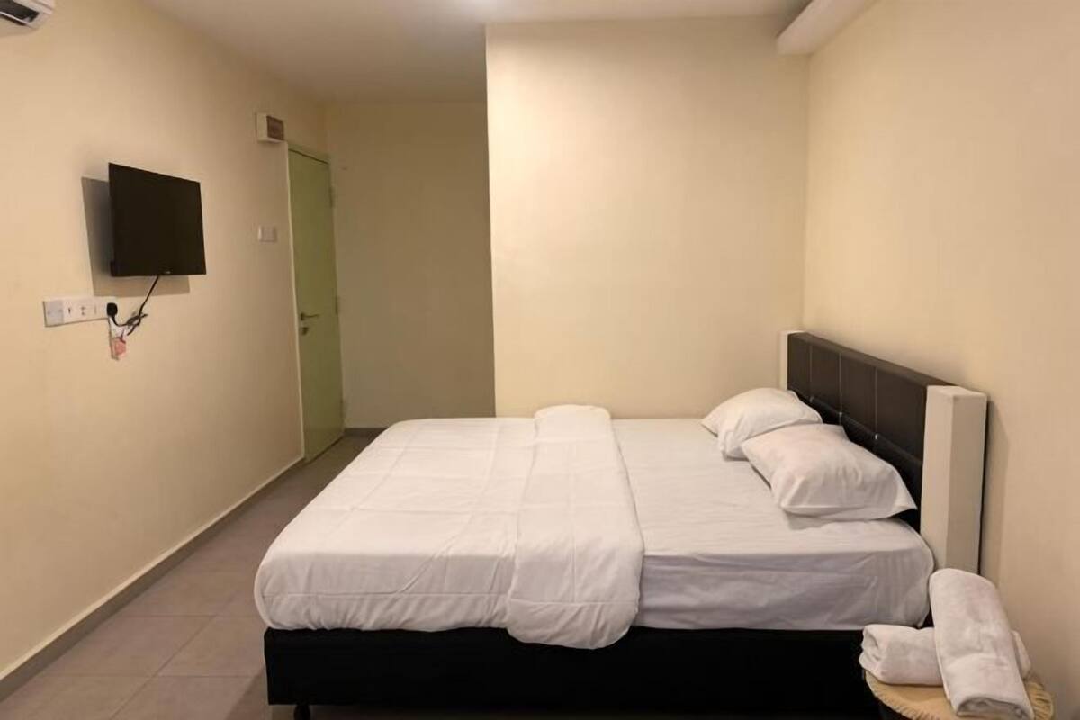 A hotel room with a bed, a flat-screen TV mounted on the wall, and a door leading to another room.