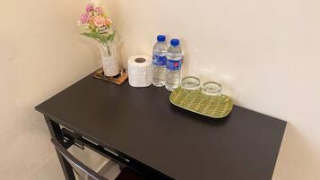 Una pequeña mesa con un florero, un rollo de papel higiénico, dos botellas de agua y dos vasos sobre una bandeja.