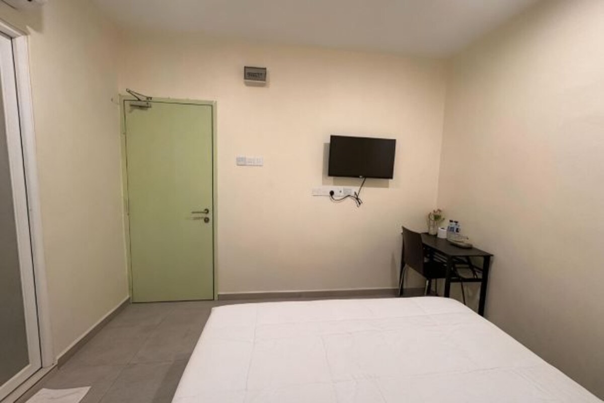 Une pièce avec un lit, une porte verte, un téléviseur fixé au mur et un petit bureau avec une chaise.