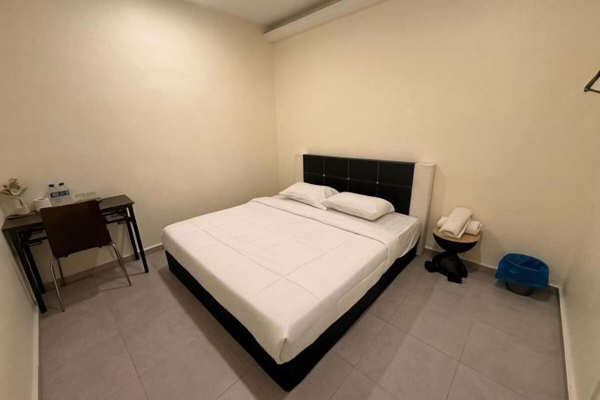 A room with a bed, a desk, a chair, a toilet, and a blue trash bin.