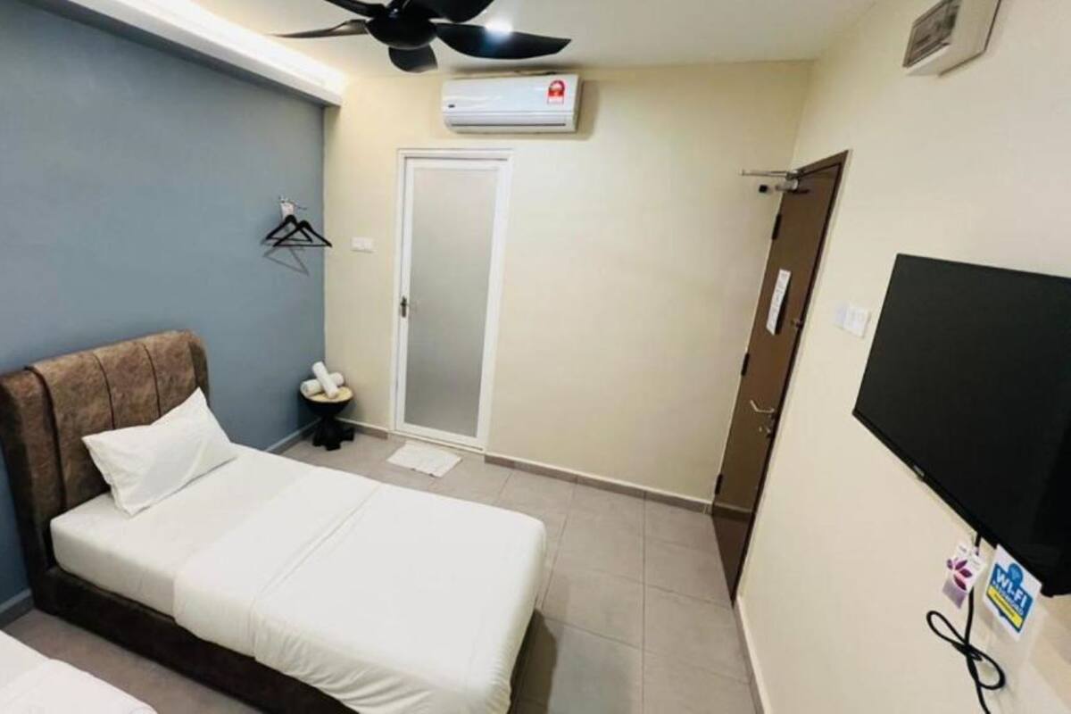 A bedroom with a bed, a ceiling fan, an air conditioning unit, a door, and a TV mounted on the wall.