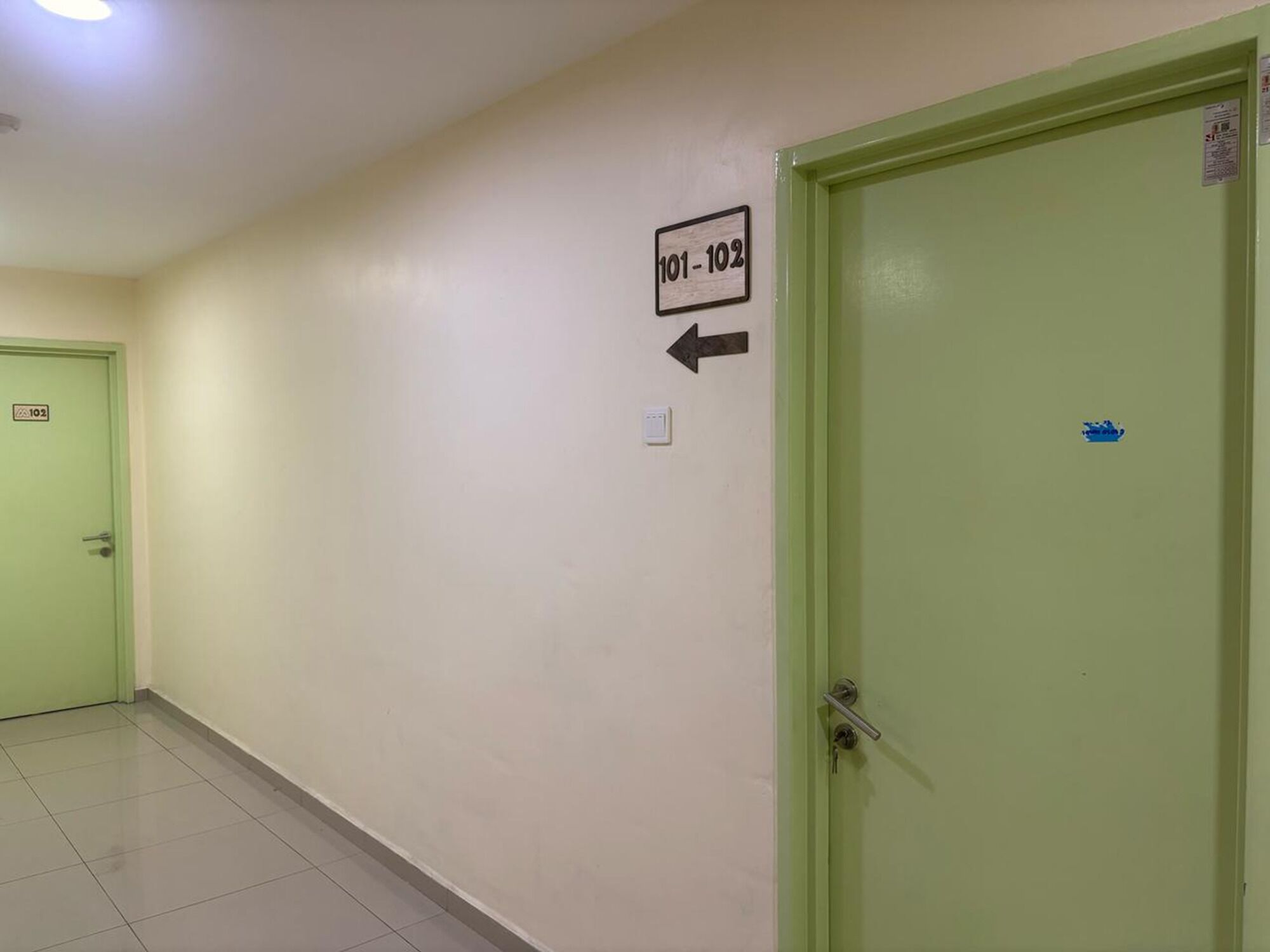 A hallway with a green door labeled 101-102, a light switch, and a door with a blue sticker.