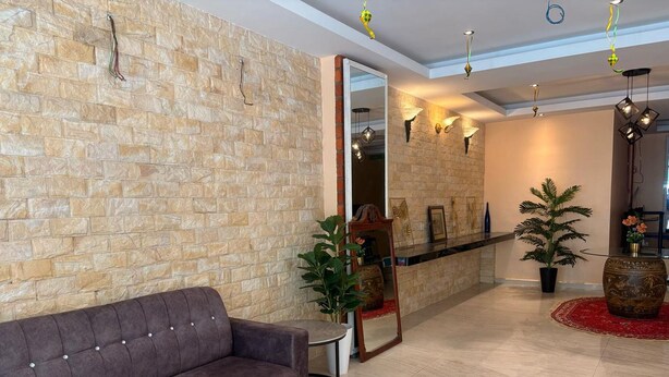 A modern lobby with a stone wall, a plush sofa, a round table, and a mirror. - Aman Inn Hotel (Malacca City)