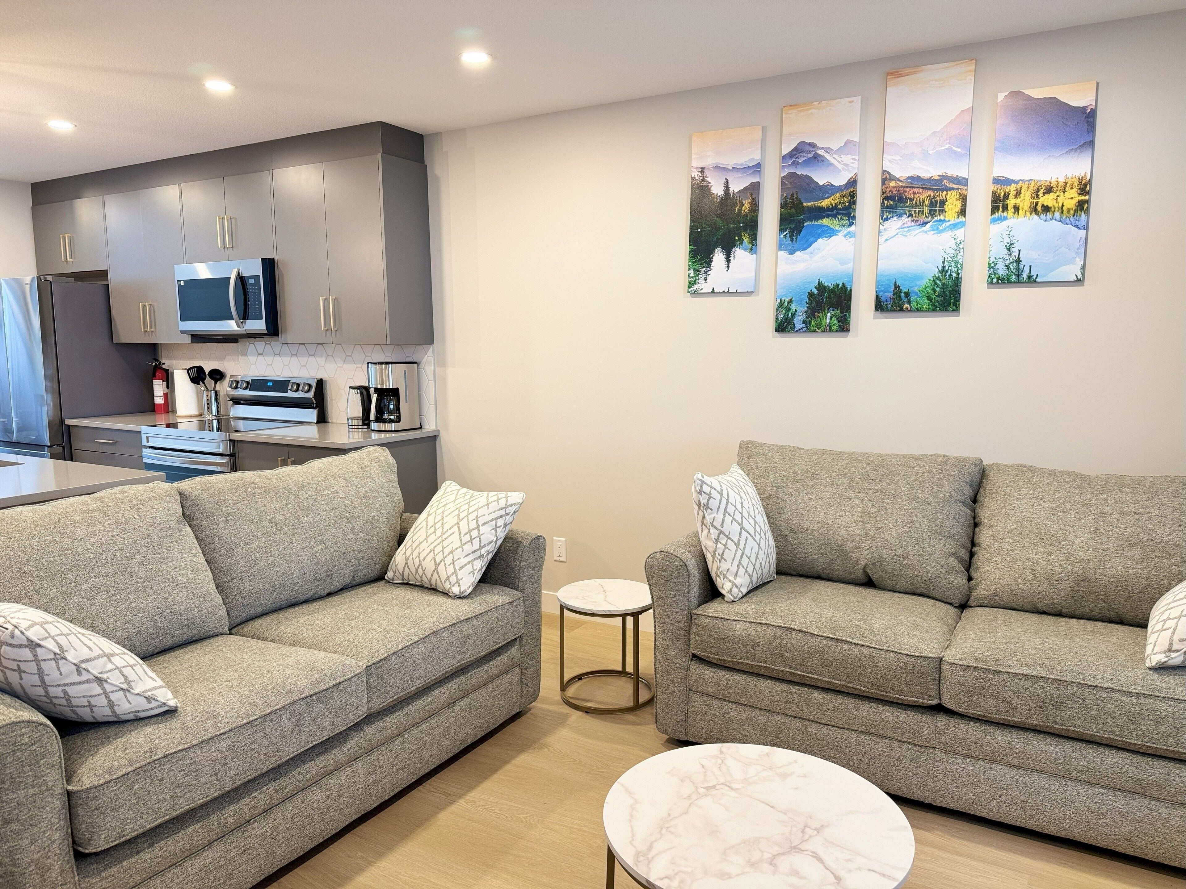 Ein modernes Wohnzimmer mit zwei grauen Sofas, einem kleinen runden Couchtisch und einer Küchenzeile mit grauen Schränken und Edelstahlgeräten.