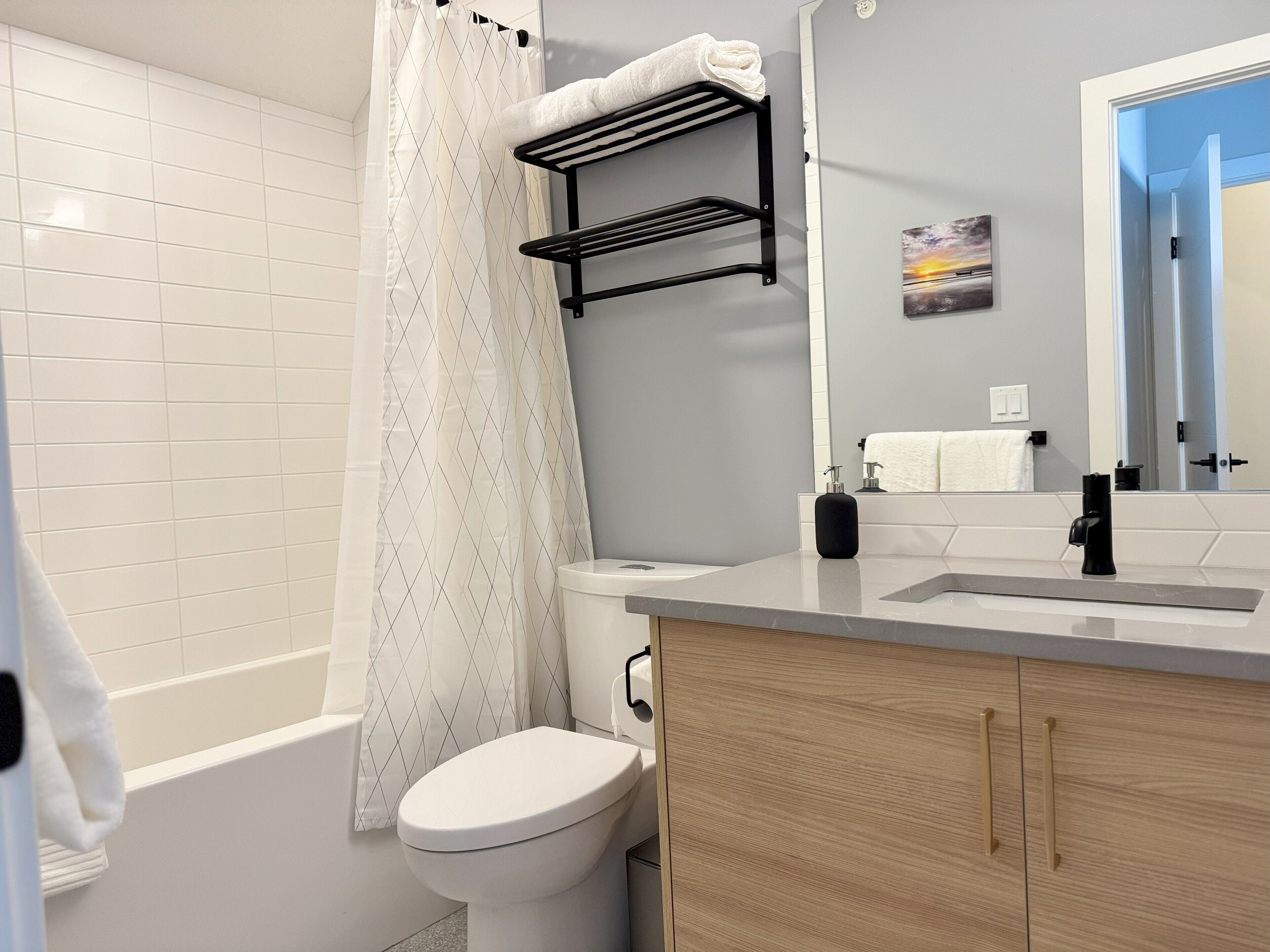 Un baño moderno con bañera, inodoro y lavamanos. Hay un perchero sobre el lavamanos y una cortina de ducha.