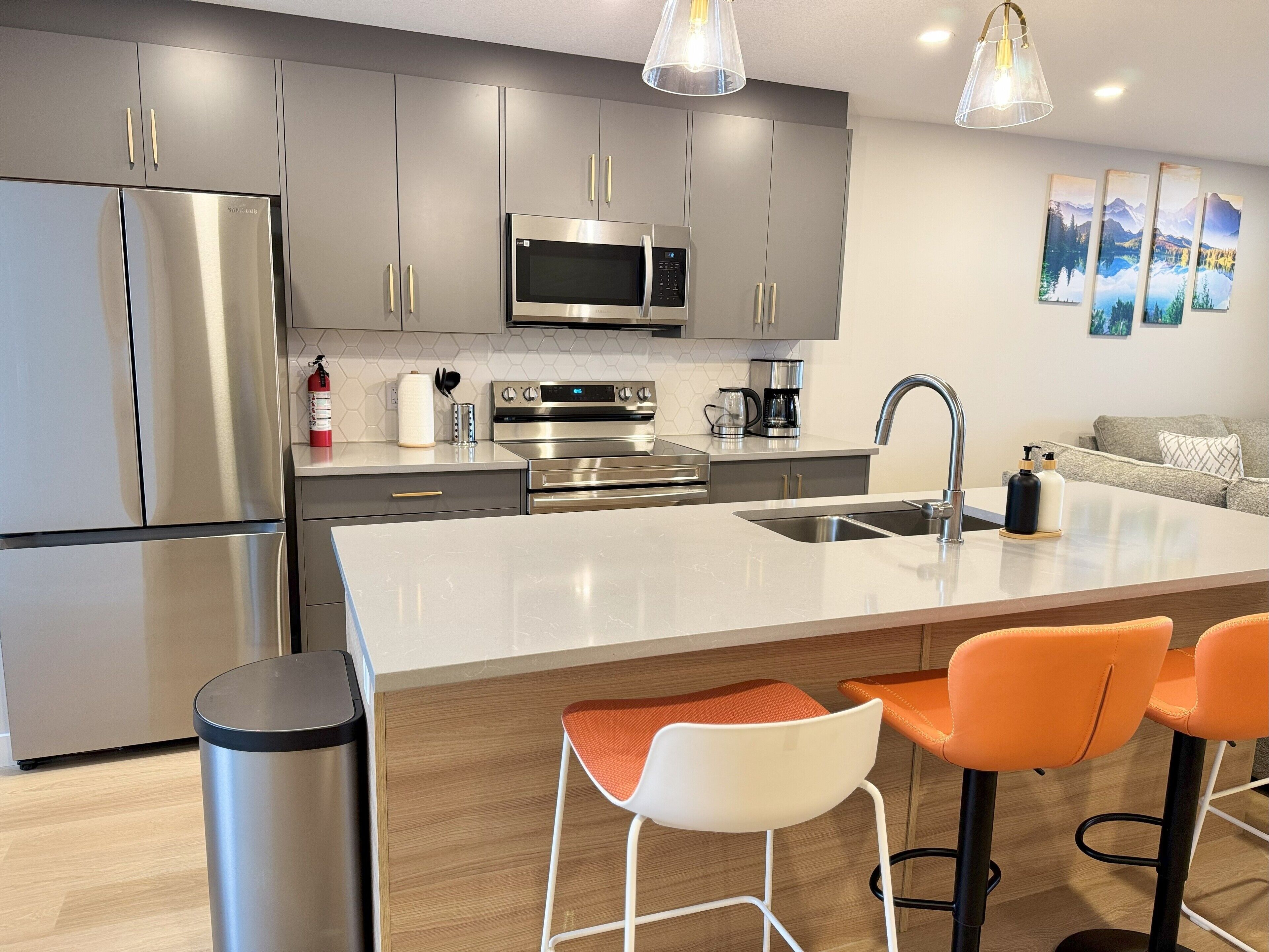 A modern kitchen with stainless steel appliances, a large island with bar stools, and a dining area with a sofa.